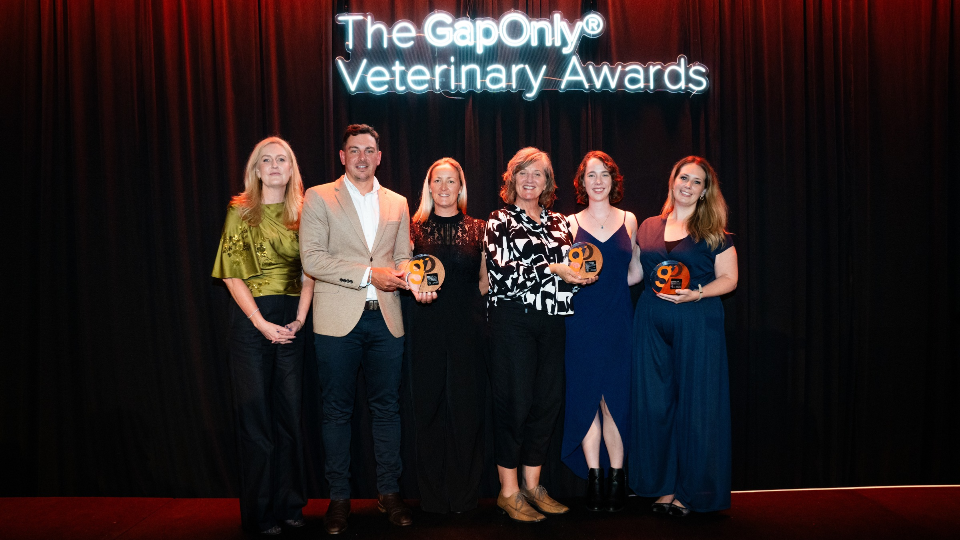 Winners of the 2025 GapOnly® Veterinary Awards standing together on stage, holding their awards, with a neon-lit sign reading "The GapOnly® Veterinary Awards" in the background.